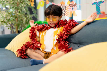 Portrait of little boy playing with red tinsel on a couch at home.の写真素材