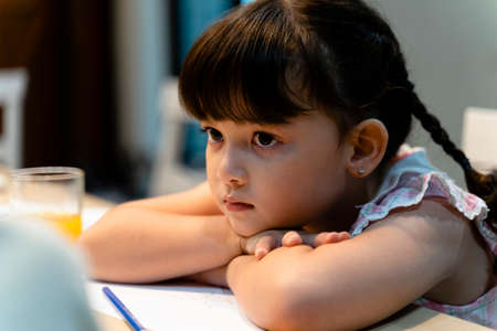 Pretty little girl tired of doing homework at kitchen table.の写真素材