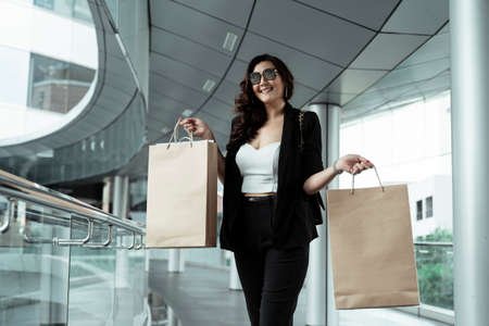 Cheerful asian businesswoman wearing sunglasses holding paper bag - shopping concept.の写真素材