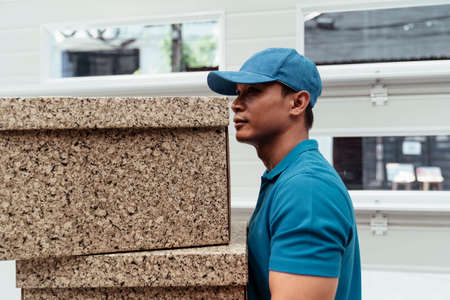 Side view- Asian male postal delivery courier man on blue working costume carrying two boxes infront of the house.の写真素材