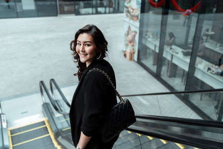 Cheerful businesswoman on black formal dress standing on escalator.の写真素材