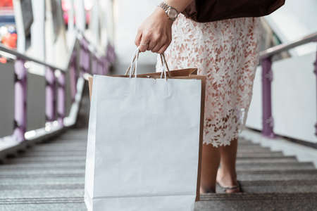 Close up hand of woman holding white shopping bag walking down stair. Copy space or blank space.の写真素材
