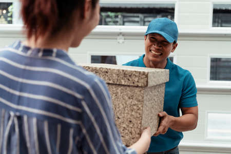 A man carrying package to customer with smile on his face - courier service concept.の写真素材