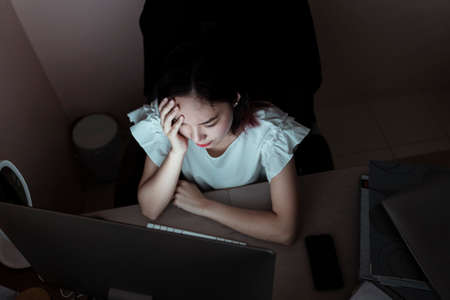 Stressful asian businesswoman working in the office infront of computer until midnight. Unhealthy condition. Migraine and Headache.の写真素材