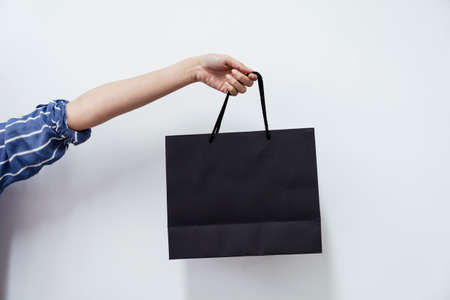 Woman hand holding black shopping paper bag with one hand isolated on white background.の写真素材