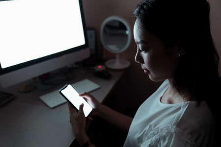 Asian woman working infront of the computer at night, using smartphone for working. Copy space.の写真素材