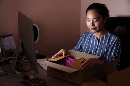 Asian woman opening shipment box infront of computer in the room - delivery service concept.の写真素材