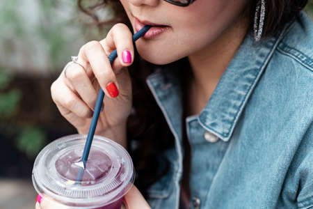 Close up asian thai woman on jeans jacket drinking grape soda water from plastic cup with straw.の写真素材