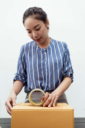 Asian thai woman packing shipment package box with transparency tape. Delivery service concept.の写真素材