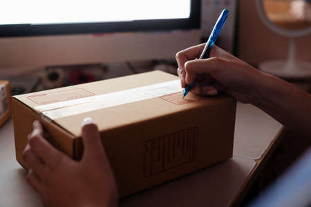 Hand of woman writing address on cardboard box with blue penの写真素材
