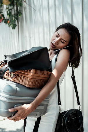 Busy asian woman carrying many heavy bags and luggages while talking on the phone. Multitasking skill.の写真素材