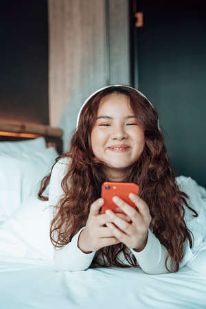 Young asian woman listen to music with wireless headphone and smartphone in bedroom.の写真素材