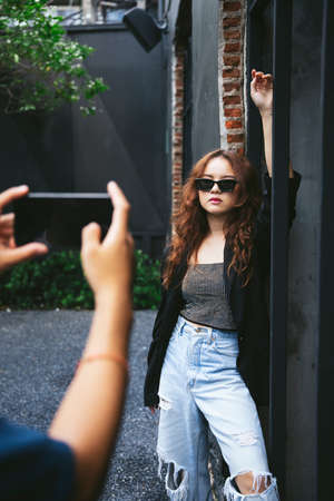 Fashion portrait of young asian woman being photographed by photograhper with smartphone.の写真素材