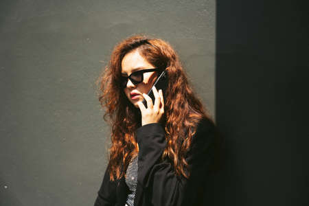 Fashion portrait of young asian woman wearing sunglasses and black jacket using smartphone.の写真素材