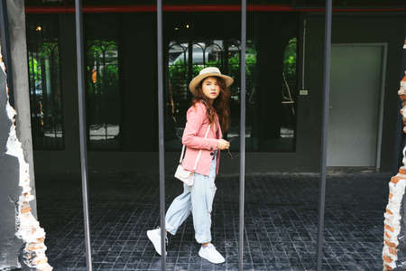 Fashion portrait of young asian woman wearing pink jacket and hat walking on street.