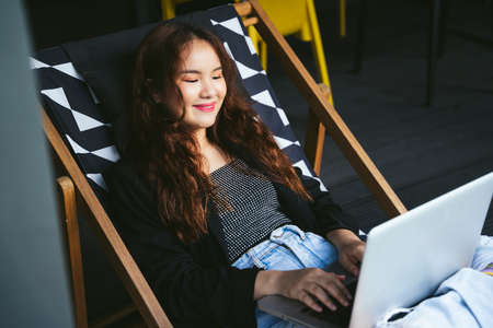 Young asian woman using laptop computer on chair beach in lounge.