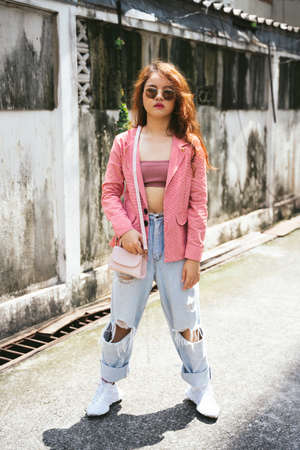 Fashion portrait of young asian woman wearing sunglasses and pink jacket on street.の写真素材