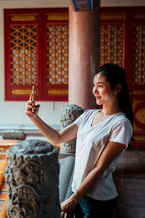 Sexy young asian womna using smartphone, taking selfie, doing vlog by smartphone, in Chinese temple.の写真素材