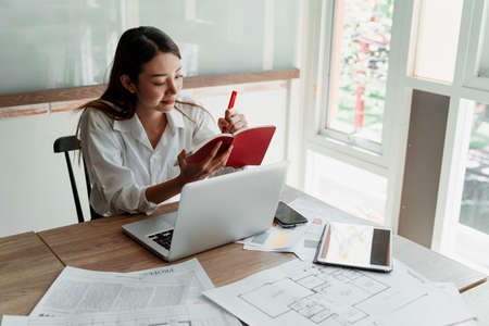 Long hair designer woman in white shirt sitting in the office take the note into red notebook while she get the great idea.の写真素材