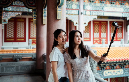 Two young asian women doing vlog video by action camera on selfie stick together with smile.の写真素材