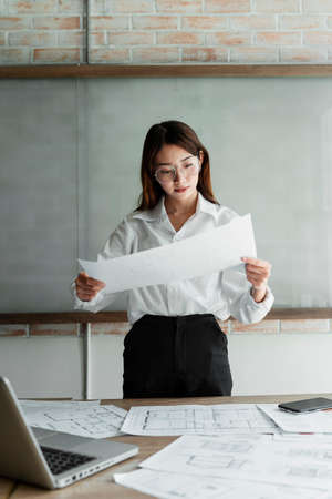 Long hair woman interior designer in white shirt hold blueprint and raise it to carefully look at the details.の写真素材