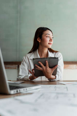 Long hair designer woman in white shirt sitting in the office searching the data of design on the...