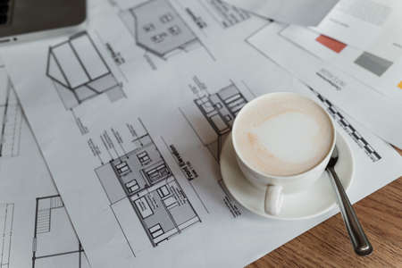 Cropped image of hot coffee with latte art in the cup on the printed blueprint and house design.の写真素材
