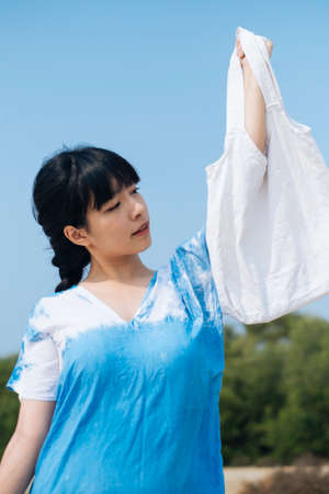 Black hair French braid girl in white and blue tie dye raise white canvas bag up.