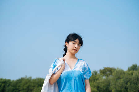Black hair French braid girl in white and blue tie dye hold canvas bag across her shoulder.の写真素材