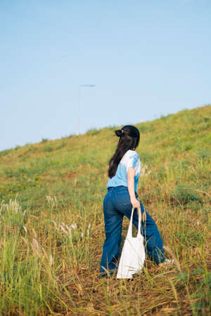 Black half tied hair girl in white and blue tie dye walk up the slope grassland and raise the canvas...