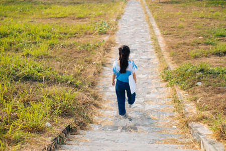 Back shot of black half tied hair girl in white and blue tie dye walk down the stone stair in the grassland.の写真素材