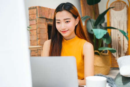 Beautiful young asian woman working on laptop computer at home.