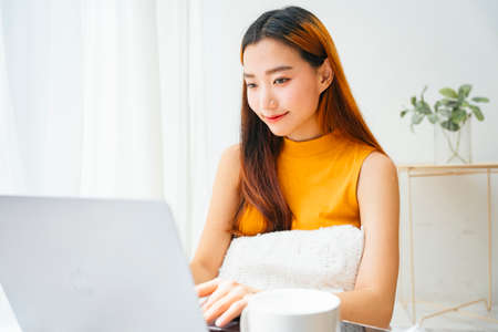 Young asian woman working on laptop computer in white room.