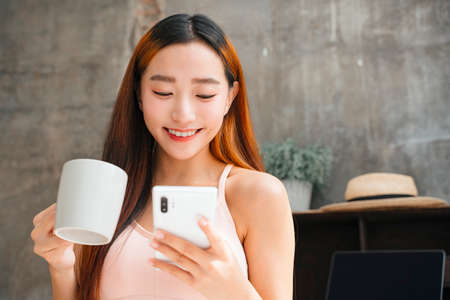 Young asian woman enjoy having coffee and watching something funny on social media.の写真素材