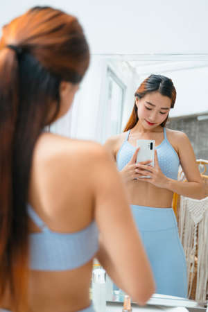 Beautiful sporty asian woman wearing sportbra taking photo at mirror. She really proud of her body.の写真素材
