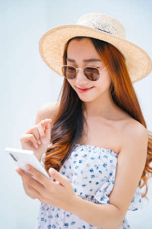 Beautiful asian traveler woman wearing sunglasses and hat using smartphone outdoors.