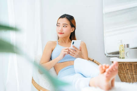 Beautiful sporty asian woman wearing sportbra using smartphone at home.の写真素材