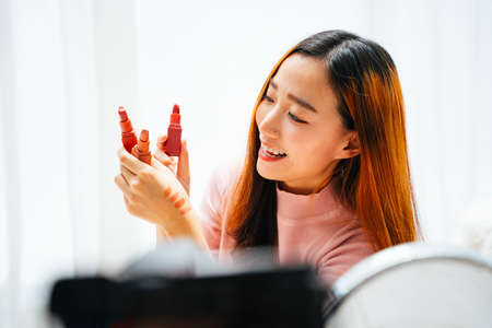 Beautiful asian woman influencer reviewing lipstick to audience on social media.