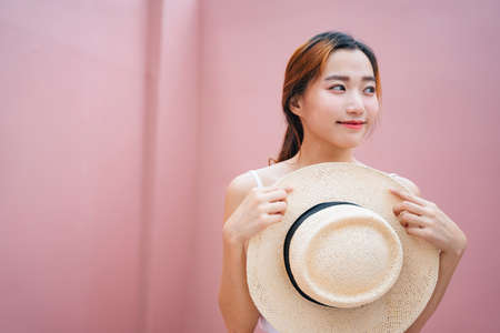 Portrait of beautiful asian woman holding straw hat on pink background.