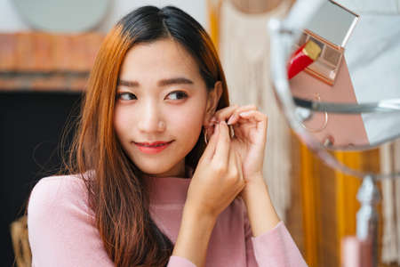 Beautiful asian woman wearing earrings infront of the mirror.の写真素材