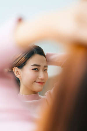 Portrait of beautiful asian woman tying hair looking at mirror.の写真素材