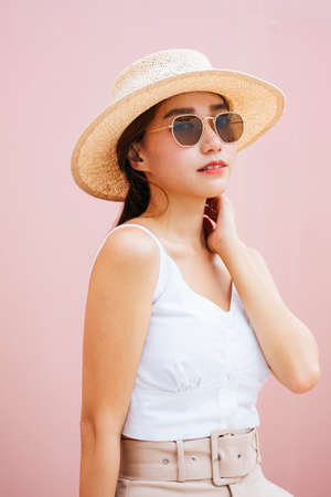 Portrait of beautiful young asian woman wearing hat and sunglasses isolated on pink background.の写真素材