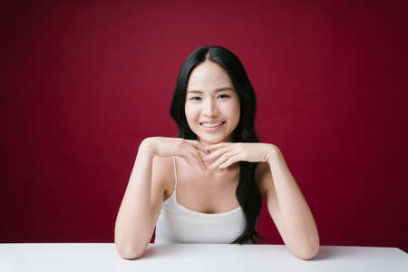 Pretty young asian woman with natural make-up looking at camera directly isolated on red background.の写真素材