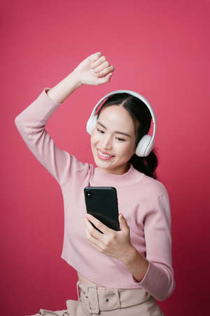Portrait of young asian woman enjoy listen to song from music streaming isolate on pink background.の写真素材