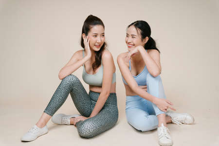 Portrait of two athlete asian sporty woman sitting together in studio light.の写真素材