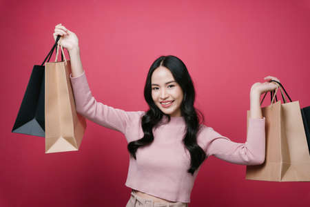 Portrait of young asian woman holding shopping paper bags isolate on pink background.