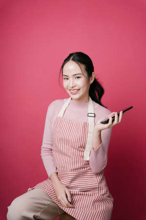 Portrait of young asian woman wearing apron using smartphone for online shopping isolate on pink background.の写真素材