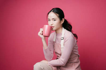 Portrait of young asian woman holding coffee mug isolate on pink background.の写真素材