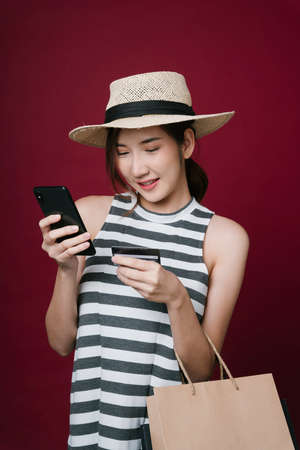 Portrait of beautiful young asian woman wearing hat using phone for online shopping with credit card.の写真素材