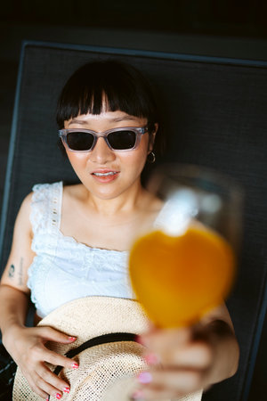Asian short hair woman wearing sunglasses enjoy orange juice at chair beach.の写真素材